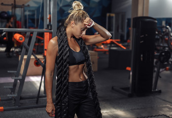 Fototapeta na wymiar Tired sport woman in sportswear with battle rope on her neck in the gym. Functional training. Healthy lifestyle concept