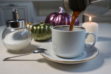 On a light table, a cup of coffee and ceramic pumpkins. Halloween