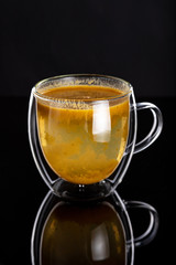 Double glass cup with homemade healthy sea-​​buckthorn tea on black background