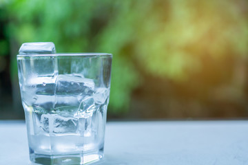 Glass with ice put on table green background of nature with copy space.