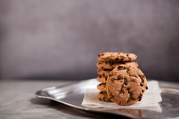 A stack of delicious round chocolate cookies on a silver tray on gray table. Bakery concept.