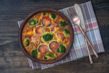 Ceramic bowl with vegetable frittata, simple vegetarian food. Frittata with egg, tomato, pepper, onion, broccoli and cheese on wooden table. Italian egg omelette