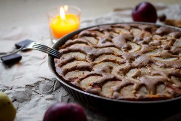 fruit pie with pears in a dish on Kraft paper, burning candle, fork in the evening