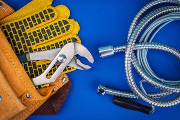 Plumbing tools and gloves for connecting water hoses on blue background