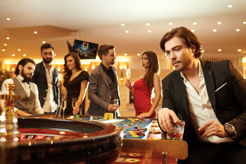 A man in a suit against the background of a roulette game in a casino.
