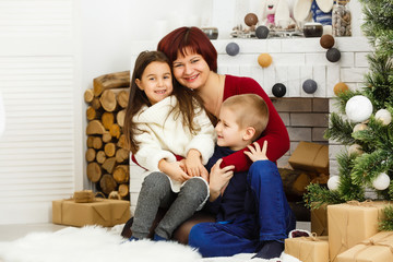 Family on Christmas eve at fireplace. Mother and little kids opening Xmas presents. Children with gift boxes. Living room with traditional fire place and decorated tree. Cozy winter evening at home.