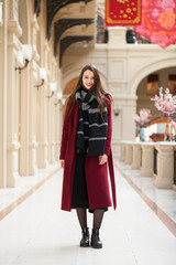 Fototapeta premium Beautiful girl in stylish in a long burgundy coat, indoor shop