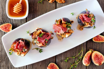 Fig appetizers with blue cheese, prosciutto and honey. Above view on a serving plate over a wood background.