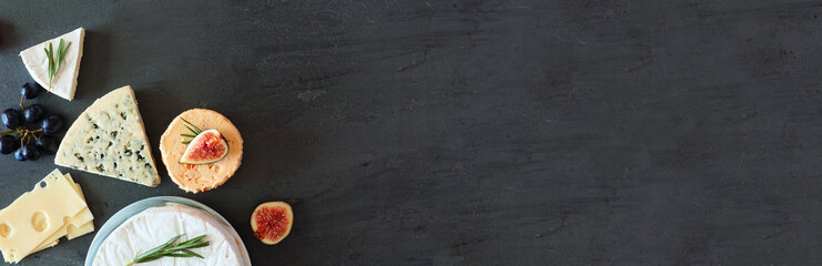 Corner border of a selection of cheeses. Top view banner on a dark stone background with copy space.
