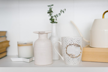 Mug, vase and candle on the shelf in the living room in white and beige colors