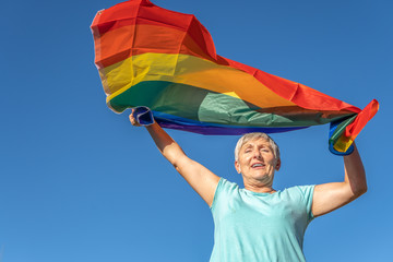 happy senior woman raising lgbt flag in blue sky background