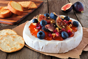 Baked brie appetizer with figs and jam, blueberries, pomegranates and nuts. Side view on a rustic wooden table.