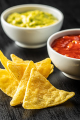 Corn nacho chips with avocado and tomato dip. Yellow tortilla chips and guacamole salsa.