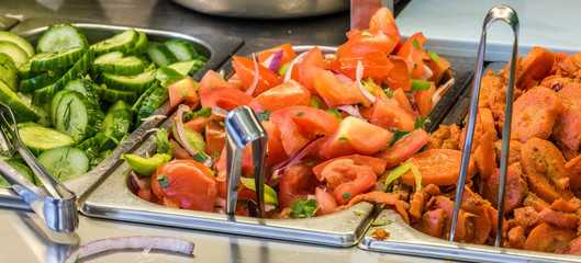 ingredients at a falafel bar with metal vegetable tongs tomatoes carrots cucumber