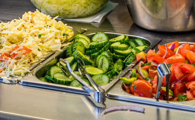 ingredients at a falafel bar with metal vegetable tongs cabbage cucumber tomatoes