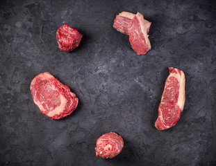 Variety of Raw Black Angus Prime meat steaks on a dark background