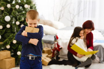 Young Boy Holding Christmas Present In Front Of Christmas Tree