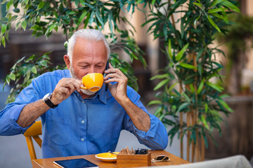 Smiling happy mature man with white stylish short beard using smartphone gadget serving internet at coffee shop cafe outdoor. Laughing old man using social media network technology feeling excited.