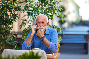 Portrait of senior man sitting in cafe and talking with smarphone. Portrait of senior man working with cellphone in outdoor cafe lounge. Man working as freelancer