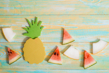 Naklejka na ściany i meble Pieces of watermelon and melon. Bright toy pineapplen on blue and yellow old wooden background. Summer concept. Flat lay, top view, copy space.