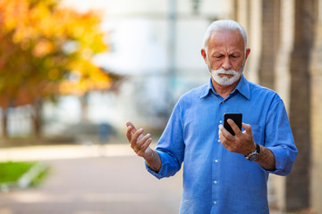 Handsome senior man using smartphone sending message stressed with hand on head, shocked with shame and surprise face, angry and frustrated. Fear and upset for mistake.