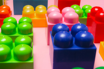 Top view of multicolor toy bricks on a pink background. Close up. Children toys.
