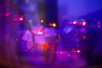 Fototapeta na wymiar small christmas present box in violet-blue light of garlands