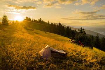 Drone photo with couple watching a beautiful sunset on a mountain with their tent and mountain bikes aside © roibu