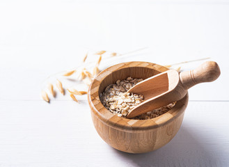 Oat flakes in sack with wood spoon on the white wooden table, macro