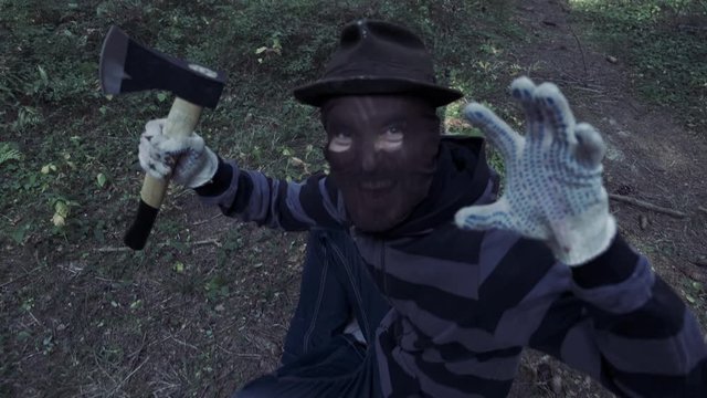Serial maniac with axe in forest, bloody killer, murderer, mad man in scary mask outdoor,  Halloween costume, horror concept.