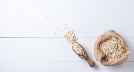 Oat flakes in sack with wood spoon on the white wooden table