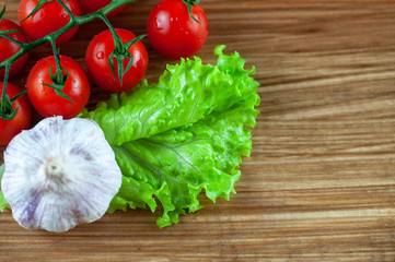 cherry tomatoes with garlic and lettuce on wooden background