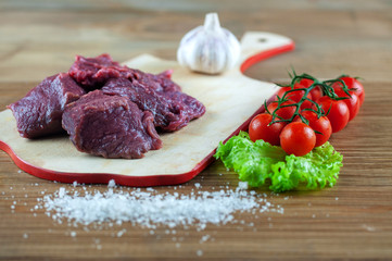 fresh meat on a chopping Board with cherry tomatoes, lettuce, garlic and seasonings