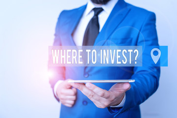 Writing note showing Where To Invest Question. Business concept for asking someone about place to put money into Businessman in blue suite with a tie holds lap top in hands