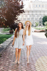 Two happy smiling girls are walking in the sunny city. Beautiful blonde and brunette walking down the street, students, travelers