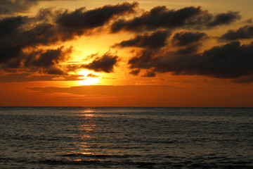 Sunset over the sea, orange sun reflected in black water. Colorful dramatic sky with dark clouds, romantic background for travel and vacations