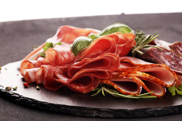 Marble cutting board with prosciutto, bacon, salami and sausages on wooden background. Rustic Meat platter
