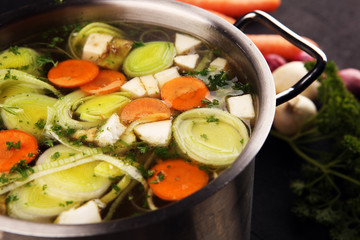 Broth with carrots, onions various fresh vegetables in a pot - colorful fresh clear spring soup. Rural kitchen scenery vegetarian broth