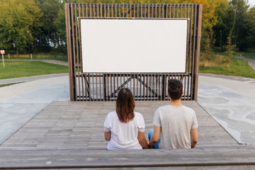 The guy and the girl in the park on the background of an open-air cinema