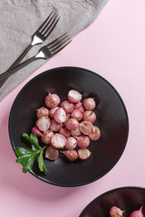 Beautiful roasted radishes in a black plate on pink table close up.