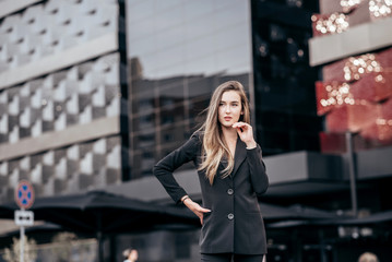Young and attractive business girl on the background of the city in a beautiful black suit.