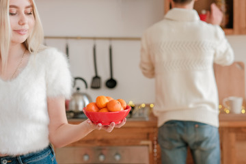 Christmas celebration. Couple setting festive table with mandarins in home kitchen.