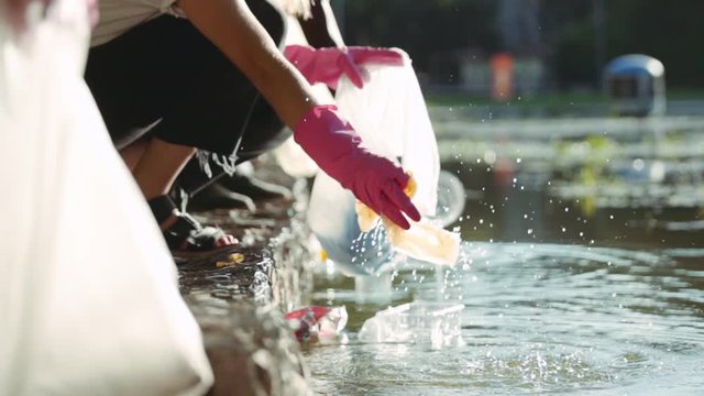 Low angle view of ecology volunteers picking up plastic trash and cleaning polluted lake in parkland. Young friendly people supporting environment conservation. Recycling concept.