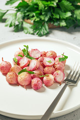 Beautiful roasted radishes in a white plate on concrete background, close up.