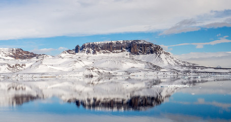 Fototapeta na wymiar Brown hill covered with snow with reflection in still water and blue sky in Antarctica