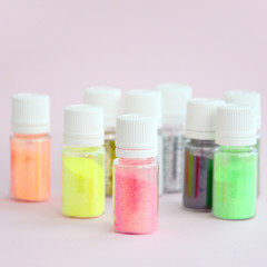 Colorful glitters lies on pastel pink background. Many round jars with multi-colored bright sparkles for nail polish