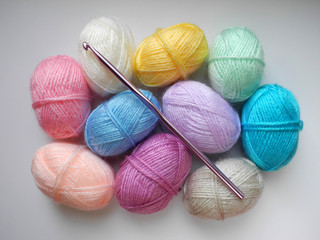 Skeins of multicolored woolen threads for knitting and crochet hook on light background