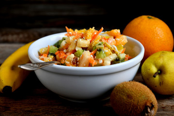 Fruit salad in a white bowl on a wooden table.