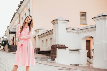 Fototapeta premium A young, beautiful girl in a pink dress walks through the beautiful streets in the city. Very beautiful portraits of a girl in the city.