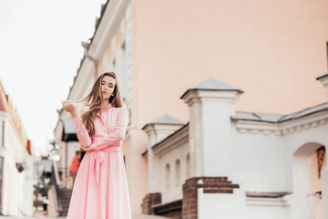 Fototapeta premium A young, beautiful girl in a pink dress walks through the beautiful streets in the city. Very beautiful portraits of a girl in the city.